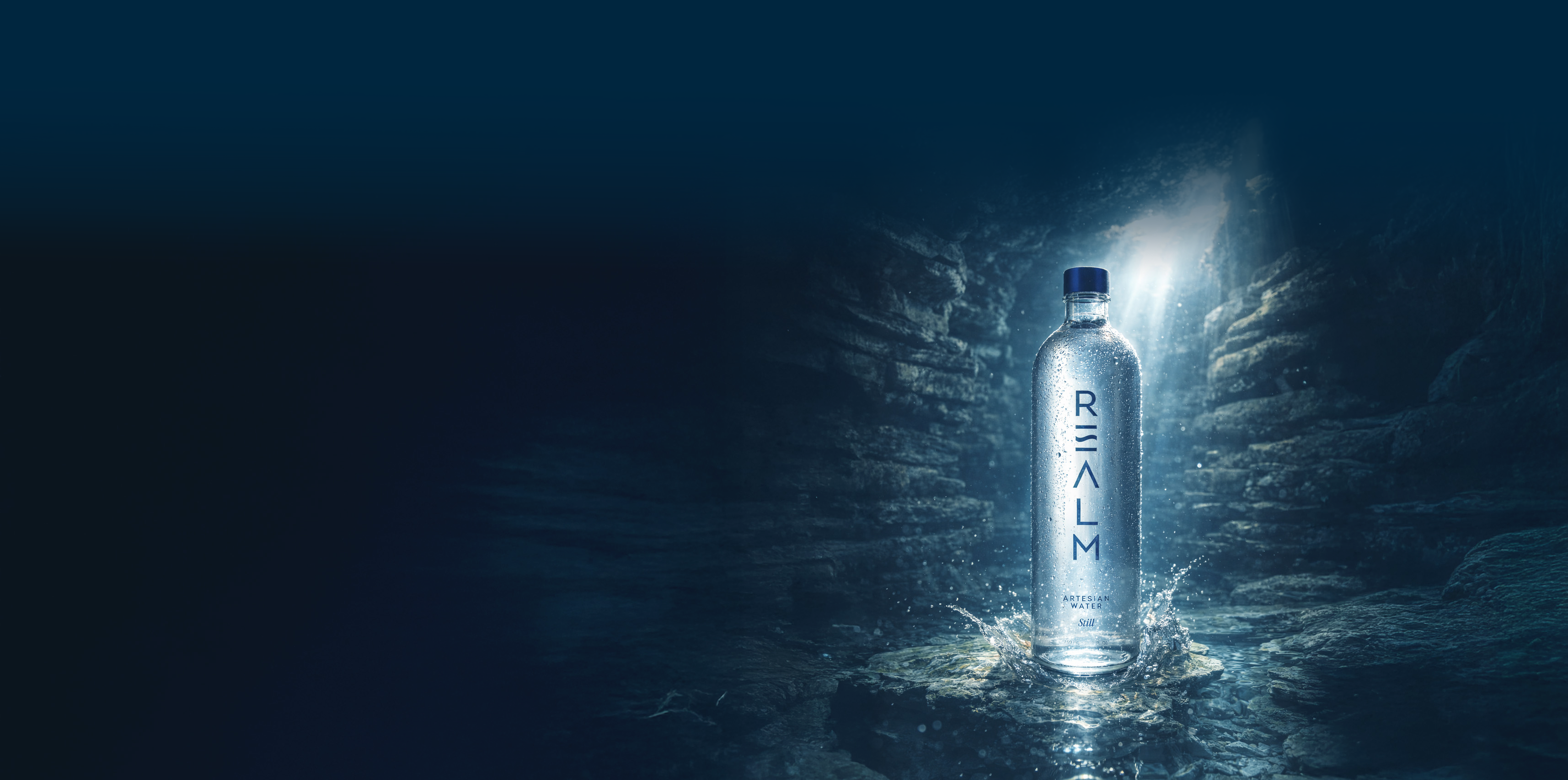 Realm Artesian Water still water bottle glowing in a dark stone cavern with light streaming from above
